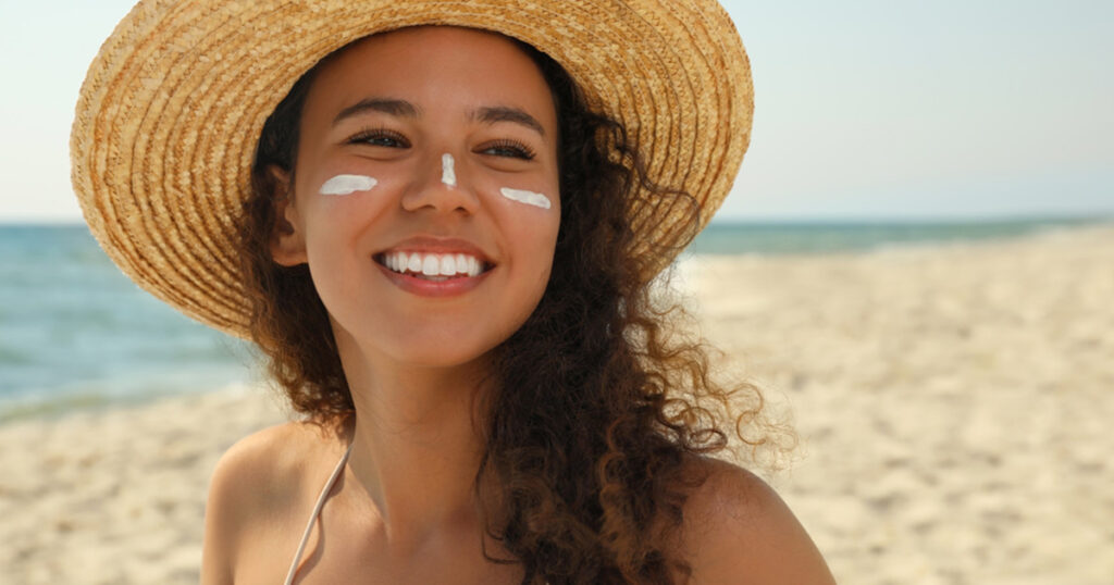 The woman has worn the hat and has applied the sun cream to her face